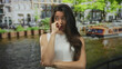 © Krakenimages.com - Young hispanic woman in a white tank top biting fingernail with anxious expression on street; anxiety.