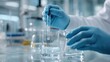 © The Little Hut - Scientist Pipetting Clear Liquid into Beaker for Experiment in Laboratory with Safety Gloves On