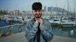 © Krakenimages.com - Young man with throat pain stands outdoors near a port with boats and water in the background, demonstrating discomfort against a nautical backdrop.