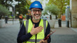 © Krakenimages.com - Man smiling in urban street wearing hardhat and safety vest while holding clipboard with colleagues in blurred background showing cheerful professional scene.