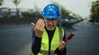 © Krakenimages.com - Man in construction vest and hard hat holding clipboard on city street background.