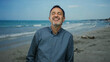 © Krakenimages.com - Middle-aged hispanic man smiling and sticking his tongue out at the beach with the sea in the background wearing a checkered shirt.