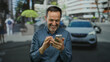 © Krakenimages.com - Man smiling while using smartphone in urban park setting, combining the joy of technology with an outdoor city environment, highlighting a middle-aged hispanic perspective.