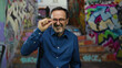 © Krakenimages.com - Middle-aged hispanic man gesturing small size while standing on an urban graffiti-covered stairway in a city park with a confident expression.