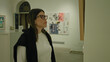 © Krakenimages.com - Woman admiring art in a gallery room, wearing glasses and dressed casually, expressing interest and contemplation in a modern exhibition space.