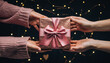 © Nai - Hands exchanging a gift wrapped with a pink ribbon during a festive occasion in a dimly lit setting with lights