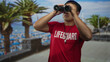 © Krakenimages.com - Lifeguard man holds binoculars to eyes in street by seaside scanning horizon; vigilance duty focus commitment.