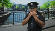 © Krakenimages.com - Policeman in uniform holds hands out near canal on a city street by iron railing with badge visible; cooperation.
