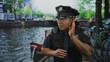 © Krakenimages.com - Man in police uniform cups ear listening to canal water by a bustling city street under sunlight; vigilance.