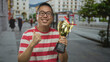 © Krakenimages.com - Man holding gold trophy on a city street wearing red striped shirt and glasses, smiling with both hands on cup; pride achievement winner.
