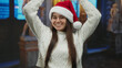 © Krakenimages.com - Hispanic woman wearing santa hat makes heart gesture with hands in a museum setting during holiday season inside a cozy indoor space featuring statues and art displays.