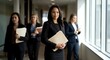 © Yuliia - Professional businesswoman leading team in modern office corridor holding documents with confident expression and diverse colleagues in background.