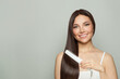 © artmim - Pretty woman brunette with long straight smooth hairstyle using hair straightener iron on light grey background