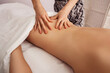 © timofeev - Close-up of a therapist hands applying firm pressure to a woman lower back and hips during a relaxing spa massage, soft warm light on smooth skin and white towel backdrop