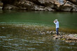 © Connect Images - Person fishing on rocky riverbank with forested cliff in background. Li River, Li Jiang, Guangxi, China