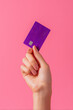 © Lady O - Hand holding a purple credit card on a pink background, a mockup template for online shopping or digital marketing concepts.