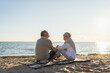 © Юлия Завалишина - Senior mature couple sitting on beach holding hands enjoying outdoor recreation. Old husband wife touching hands with tenderness love. Grandmother grandfather together. Family moment of love