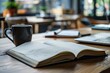 © juliars - Open notebook with handwritten notes, coffee mug, laptop, and notepad on a wooden table in a cafe, suggesting working or studying