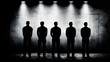 © Chaiwit - Silhouettes of five men standing in lineup under bright spotlights against textured wall, creating dramatic and tense atmosphere