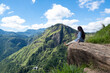 © Сергей Дудиков - A young woman sits on a rock and admires the breathtaking views from the small Adama peak near Ella, Sri Lanka. Beautiful views from the mountaintop of Ceylon. Highland Sri Lanka.