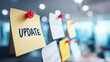 © t.sableaux - Handwritten update message on a sticky note attached to a glass board in an office setting with blurred background elements and bright lighting