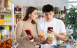 © JackF - Positive young woman and man looking to buy sauce, scans QR code from label in small food supermarket