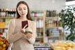 © JackF - Thoughtful young woman making purchases in local grocery store, using smartphone to scan barcode on canned food packed in tin can. Modern shopping concept