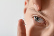 © New Africa - Man putting on contact lenses against light background, closeup. Space for text