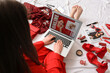© Pixel-Shot - Young woman with laptop, makeup products and different red accessories shopping online on bed, closeup