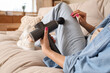 © Pixel-Shot - Young woman massaging her leg with percussive massager on sofa at home, closeup