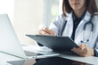 © tippapatt - Asian femal doctor writing notes on clipboard for hospital schedule, history record or healthcare checklist. Doctor writing prescription, medication document for patient in hospital office
