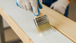 © Vertstyle - A person wearing gloves is painting a wooden plank white with a brush, showing a precise application of paint