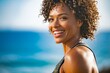 © StreamPixel - A fit woman with curly hair smiles brightly over her shoulder during an outdoor workout. The sunlight highlights her glowing skin and the ocean background suggests a coastal exercise route.