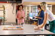 © wavebreak3 - Diverse female colleagues collaborating around table in office holding smartphone, tablet