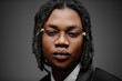 © TrueFrame Collective - Portrait of young adult Black man wearing eyeglasses looking directly at camera with neutral expression, close up of face and upper shoulders against plain background