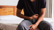 © FranKissStudio - Man Sitting on Bed Clutching Stomach with Abdominal Pain Symptoms