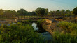 © AmazingAerialAgency - Aerial view of a sturdy steel bridge cutting across a tranquil stream, reflecting the clear sky amid the lush greenery, Derre, Zambezia Province, Mozambique.