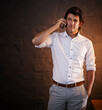 © peopleimages.com - Business man, phone call and conversation in office for networking, news or deal at night. Mobile, contact and discussion for communication, info or negotiation of broker on deadline by brick wall
