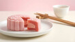© Solos - Beautiful pink snow skin mooncake with strawberry cream filling on a white plate with tea.