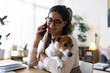 © Studio Marmellata - A woman wearing glasses smiles while talking on her phone and holding her dog.