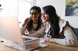 © Studio Marmellata - Two women collaborate on a project, one holding a pencil to her mouth while looking at a laptop screen, the other focused on a notebook.