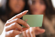 © Studio Marmellata - A person holds a green payment card with a chip and embossed text. The card is the focus of the image, with blurred figures in the background.