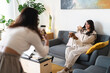 © Studio Marmellata - A woman films her dog on her phone while sitting on a sofa in a bright, modern living room with plants and artwork.