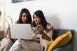 © Studio Marmellata - Two women and a dog are sitting on a couch, looking at a laptop together.
