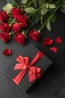 © Anastasiia Kasina - Black gift box with red bow and red rose flowers on the black background, top view