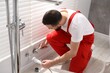 © New Africa - Plumber in uniform working near window indoors