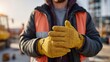 © imagemir - Male construction worker wearing a safety vest and yellow gloves, preparing for work at a construction site during sunset.