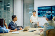 © we.bond.creations - Asian businesswoman presenting ideas and leading discussion with diverse colleagues in a modern corporate boardroom meeting