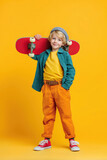 Child holds skateboard with bright colors in studio with yellow background