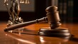 © George Louris  🜲 - Wooden gavel on table with statue of Justice and scales in background, symbolizing law & order